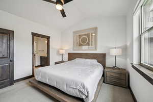 Carpeted bedroom featuring ensuite bathroom, a ceiling fan, and vaulted ceiling