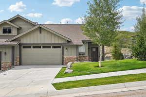 Craftsman-style house featuring roof with shingles, board and batten siding, stone siding, and concrete driveway