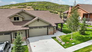 View of front facade with roof with shingles, stone siding, driveway, a front lawn, and a garage