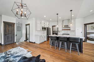 Kitchen with a center island with sink, white cabinetry, light wood-type flooring, a kitchen bar, and stainless steel appliances