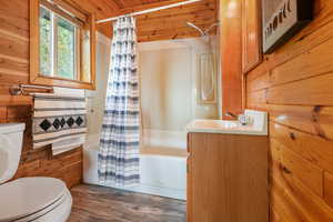 Bathroom with wood walls, shower / tub combo, vanity, dark wood-type flooring, and wooden ceiling