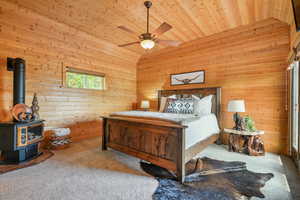 Carpeted primary bedroom featuring a wood stove, wooden walls, wood ceiling, ceiling fan, deck access and lofted ceiling