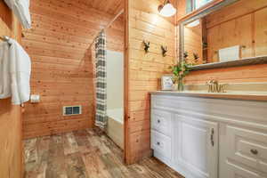 Full primary suite bathroom with wood walls, shower / bath combo, vanity, and light wood-like LVP floors