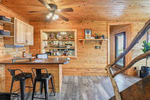 Kitchen featuring open shelves, wooden ceiling, dark countertops, a breakfast bar area, and light wood-style floors