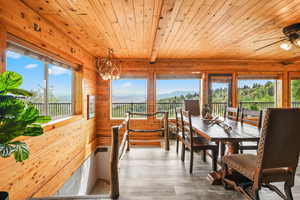 Dining room with wood-style LVP finished floors, wooden walls, a wood ceiling with exposed beams, a mountain and valley view, and a chandelier