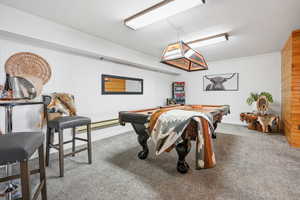 Recreation room with light carpet, billiards, wood walls, and a baseboard heating unit