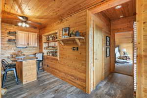 Dry bar with wood ceiling, dark wood-style flooring, a ceiling fan, and wood walls