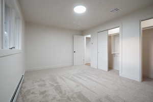 Unfurnished bedroom featuring baseboard heating, light colored carpet, and multiple closets