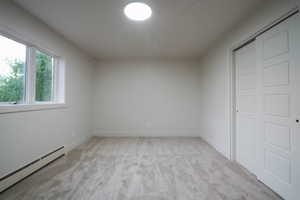 Unfurnished bedroom featuring a baseboard heating unit, light carpet, and a closet