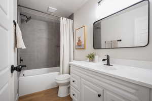 Bathroom featuring vanity, shower / bathtub combination with curtain, light wood finished floors, and a textured ceiling