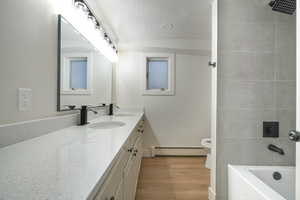 Bathroom with double vanity, a textured ceiling, light wood-style floors, a baseboard radiator, and bathing tub / shower combination