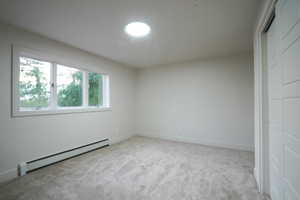Unfurnished bedroom featuring a baseboard radiator, light carpet, and a closet
