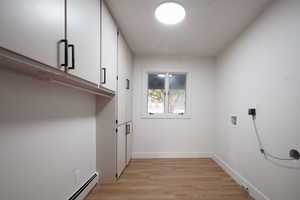 Laundry room featuring light wood-style flooring, a baseboard heating unit, hookup for a washing machine, and cabinet space