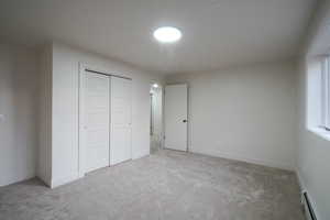 Unfurnished bedroom with a closet, a baseboard heating unit, and carpet flooring