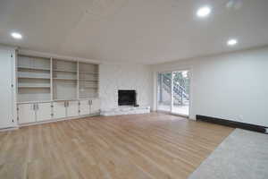 Unfurnished living room featuring light wood-style floors, recessed lighting, a fireplace, and a baseboard radiator