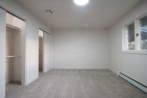 Unfurnished bedroom featuring a baseboard heating unit, multiple closets, and light carpet