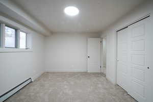 Unfurnished bedroom featuring a baseboard heating unit, light carpet, and a closet