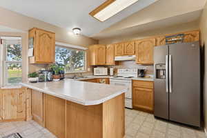 Kitchen with white appliances, light flooring, lofted ceiling, light countertops, and a peninsula