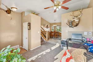 Carpeted living area featuring a ceiling fan, a chandelier, lofted ceiling, and stairway