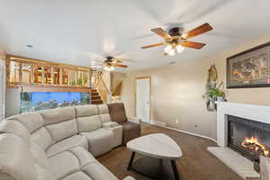 Carpeted living area featuring a ceiling fan, a fireplace, and stairway