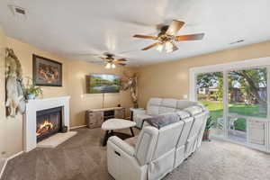 Carpeted living room featuring ceiling fan and a fireplace