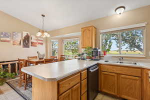 Kitchen featuring stainless steel dishwasher, light countertops, a peninsula, pendant lighting, and a chandelier