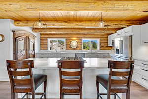 Kitchen featuring light wood-style flooring, pendant lighting, log walls, white cabinets, and a wooden ceiling with exposed beams