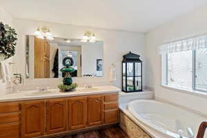 Bathroom with double vanity, a bath, and dark wood-style flooring