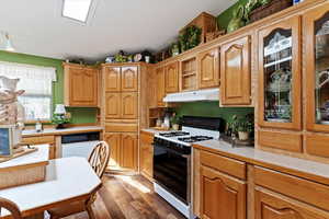 Kitchen featuring light countertops, white appliances, dark wood finished floors, under cabinet range hood, and brown cabinets