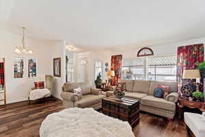 Living room featuring dark wood-style floors, a chandelier, and vaulted ceiling