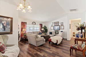 Living room with a chandelier, dark wood-style floors, and lofted ceiling