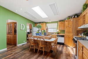 Kitchen with white appliances, light countertops, a breakfast bar area, dark wood-style flooring, and lofted ceiling