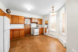 Kitchen featuring white appliances, light countertops, a baseboard radiator, and brown cabinets