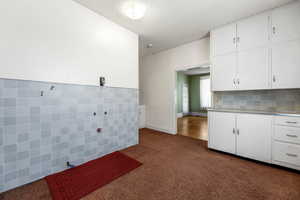 Kitchen with tile walls, a textured ceiling, white cabinets, dark colored carpet, and wainscoting