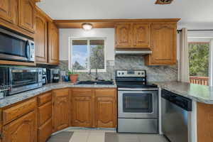 Kitchen with brown cabinetry, stainless steel appliances, decorative backsplash, and light countertops