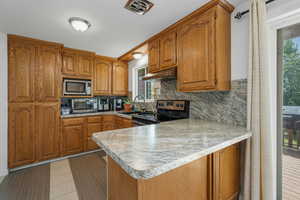 Kitchen with brown cabinets, backsplash, a peninsula, stainless steel appliances, and light countertops
