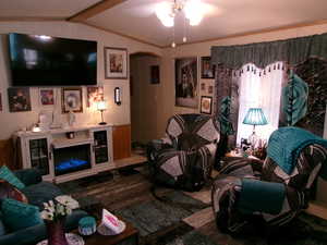 Living room featuring a fireplace, arched walkways, ceiling fan, and wood walls