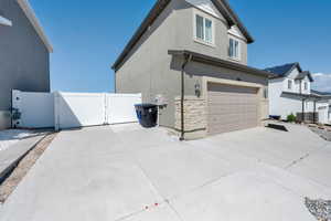 View of side of home with a gate, stucco siding, stone siding, an attached garage, and concrete driveway