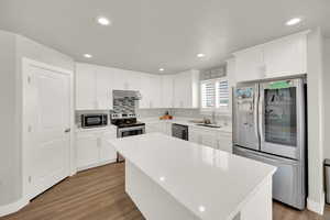 Kitchen with appliances with stainless steel finishes, white cabinetry, recessed lighting, light wood-style flooring, and backsplash