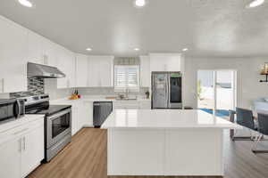 Kitchen with recessed lighting, stainless steel appliances, a kitchen island, light wood-style floors, and under cabinet range hood