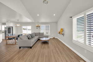 Living room featuring vaulted ceiling, a chandelier, light wood-style floors, and recessed lighting