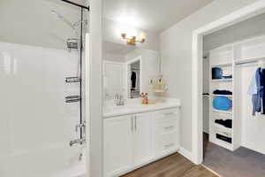Bathroom featuring washtub / shower combination, vanity, dark wood-style floors, and a walk in closet