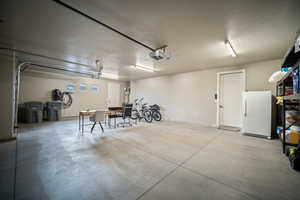 Garage with freestanding refrigerator, strapped water heater, and a garage door opener