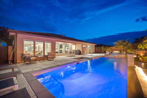 Pool at night featuring a patio area, area for grilling, a pool with connected hot tub, and a fenced backyard