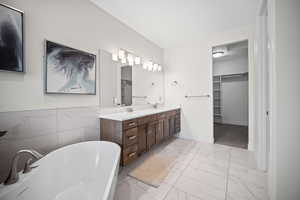 Full bathroom featuring a spacious closet, a freestanding tub, double vanity, light marble finish floors, and tile walls