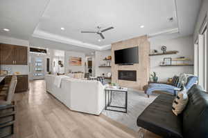 Living area featuring a tray ceiling, a tile fireplace, ceiling fan, and recessed lighting