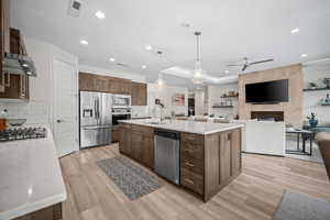 Kitchen featuring hanging light fixtures, open floor plan, appliances with stainless steel finishes, an island with sink, and light stone counters