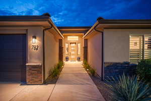Doorway to property featuring stone siding, stucco siding, an attached garage, and driveway