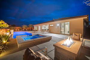 Pool at twilight featuring a patio, a pool with connected hot tub, and an outdoor living space with a fire pit