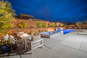 Pool at night with a patio, a fenced backyard, a pool with connected hot tub, and an outdoor living space with a fire pit